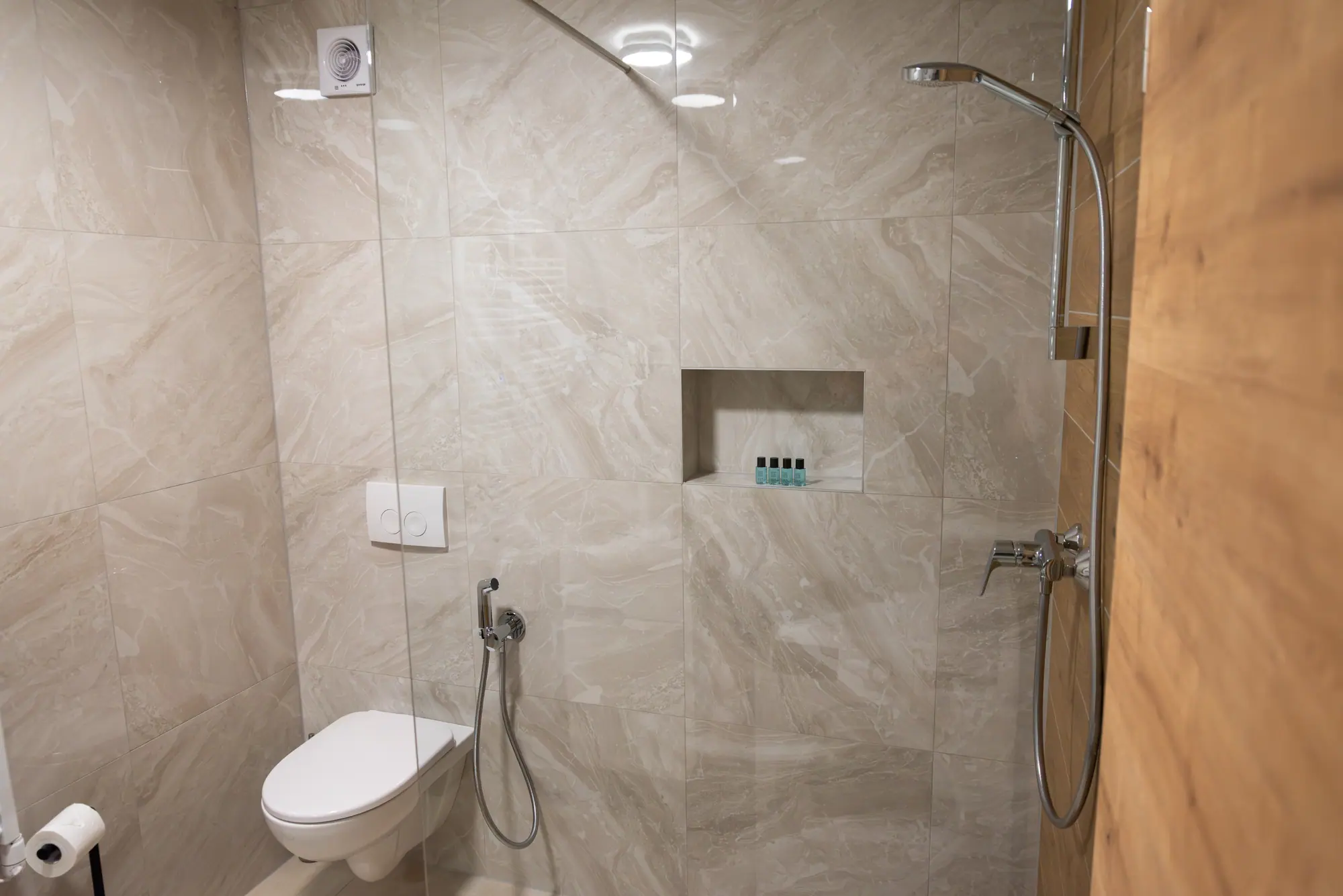 The walk-in shower in marble-toned stone, framed by an oak panel