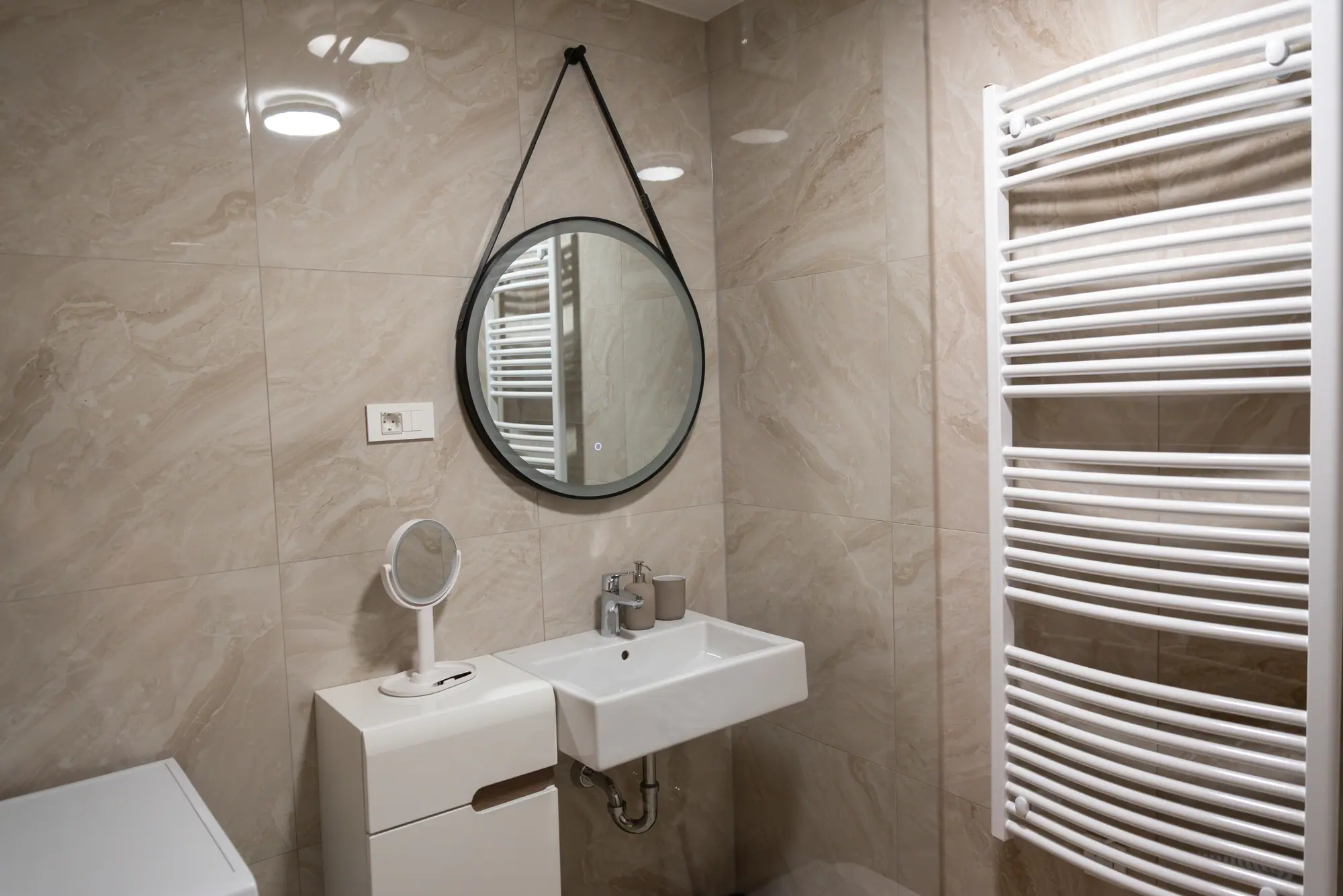 The bathroom vanity — a round leather-strap mirror and a ladder towel rail