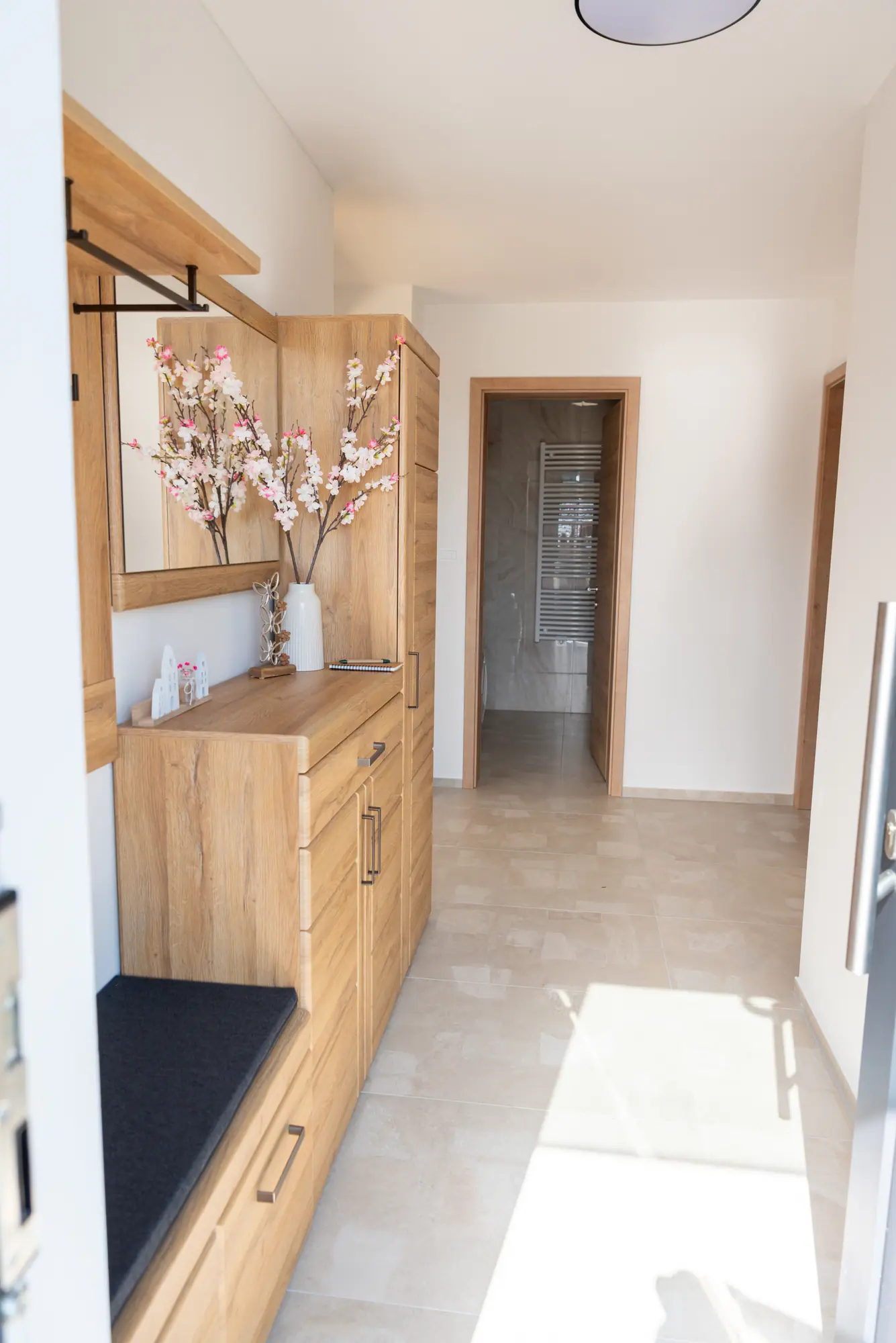 The entrance hall in oak — a stone-tiled floor, a mirror, and blossom branches