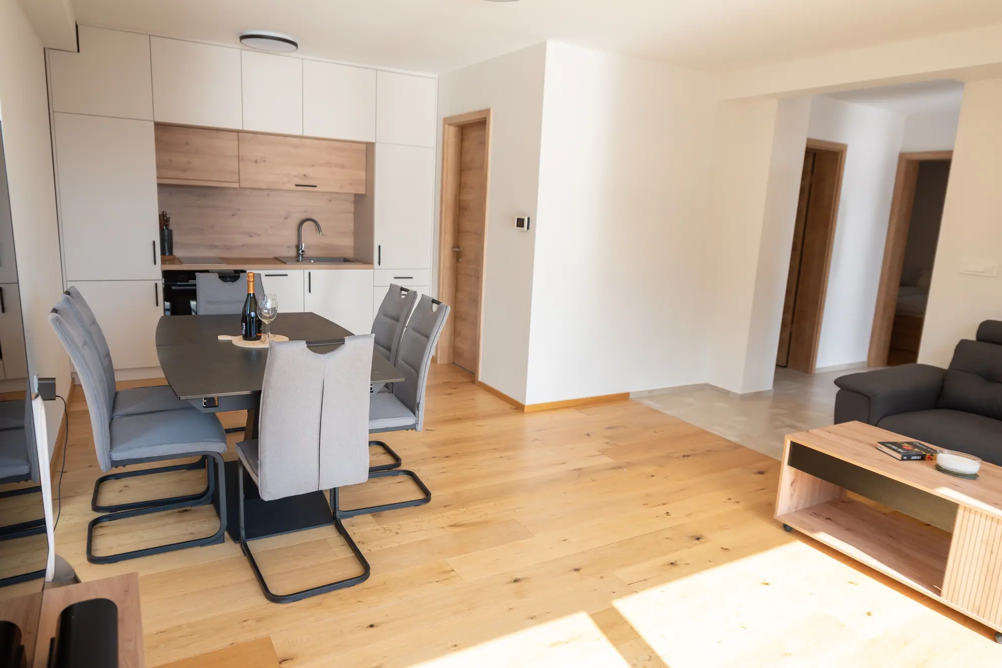 The open-plan living and dining room — oak floor, a matte-white kitchen, and oak doors through to the bedrooms
