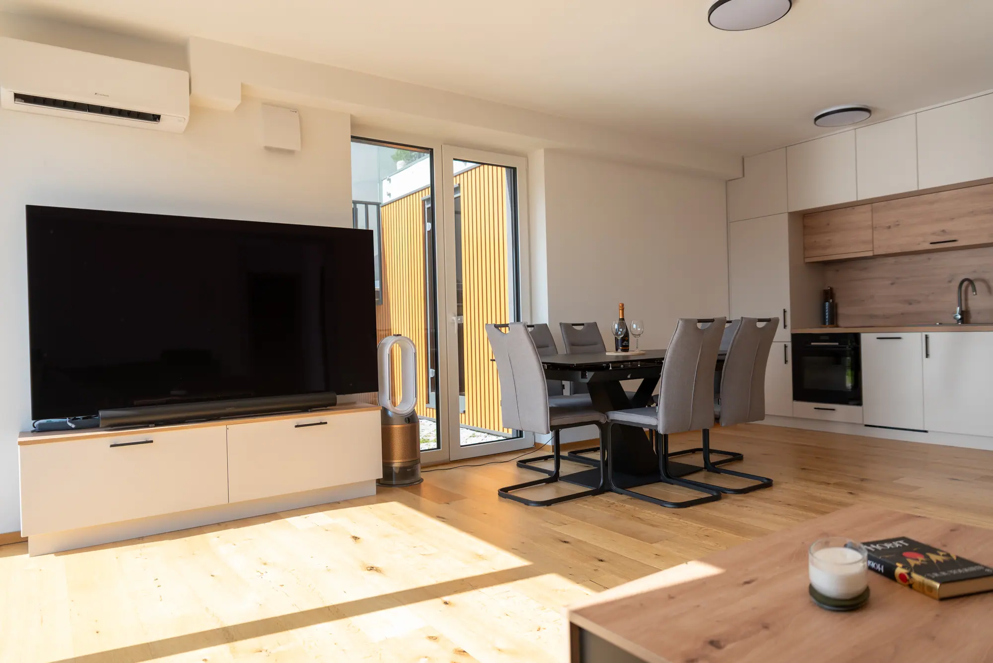 The living and dining area in afternoon light, the kitchen and balcony beyond